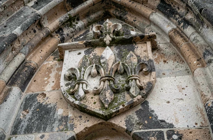 Relief en pierre sculptée sur façade de cathédrale gothique française représentant trois fleurs de lys en bouclier héraldique